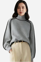 Woman wearing a soft gray Zero Itch Turtleneck Sweater with black slimming contrast trim and beige trousers
