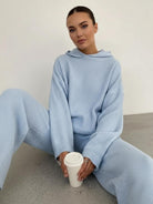 woman wearing light blue waffle-knit two-piece loungewear set with hoodie and wide-leg pants sitting on floor holding coffee cup