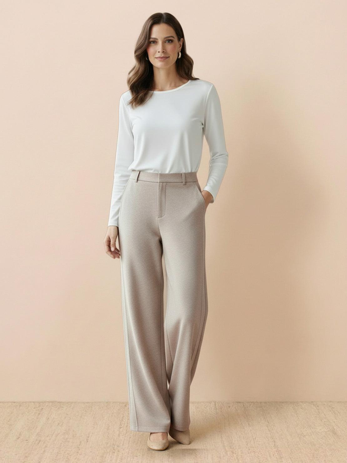 woman wearing beige wide-leg thermal wool blend trousers with white long-sleeve top standing against beige wall