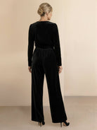 Woman wearing a deep V-neck velvet suit with long sleeves, removable waist tie, and wide-leg pants