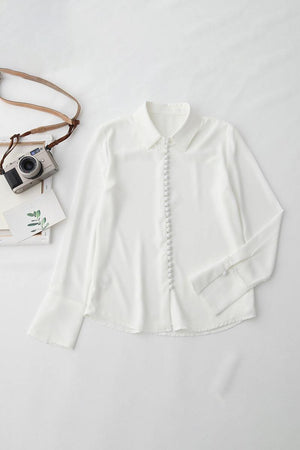 White Bayam blouse with button details, long sleeves, and classic collar, laid flat on a white surface.