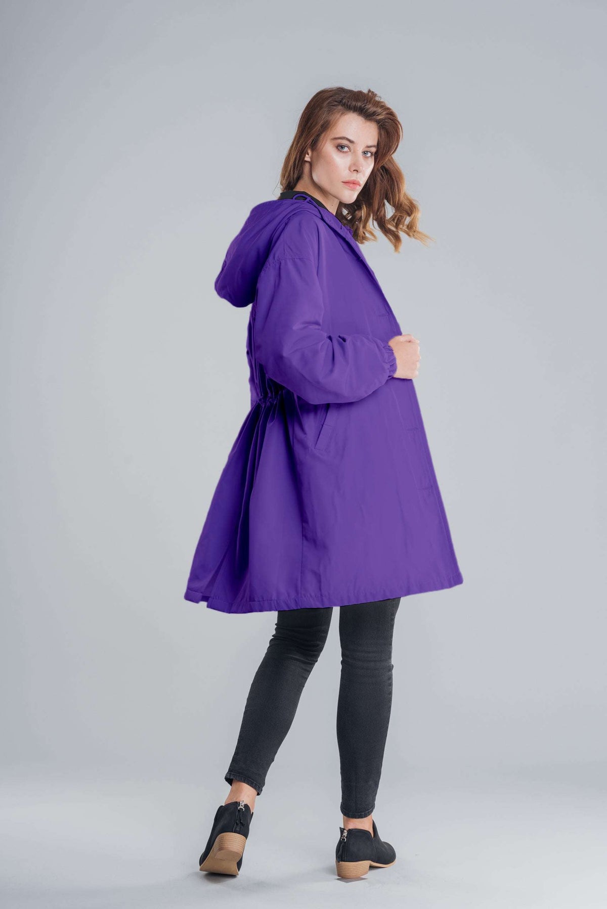 Water-resistant oversized windbreaker rain jacket in purple with hood, modeled by woman against gray background