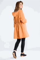 Woman wearing orange water resistant oversized windbreaker with hood and cinched waist from the back