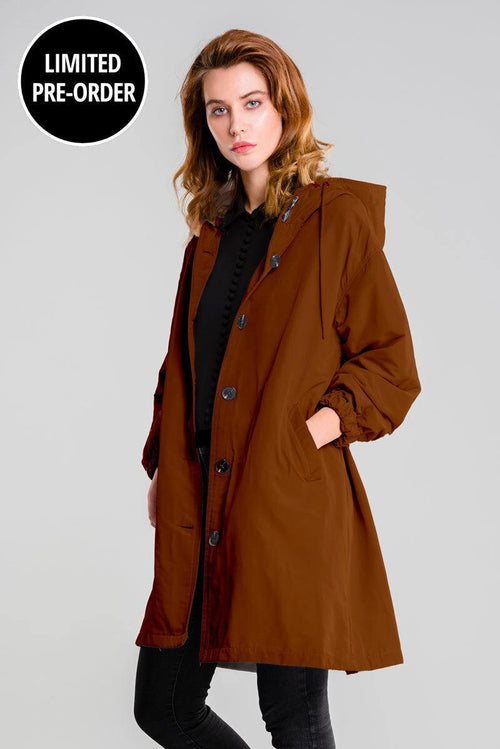 Water-resistant oversized windbreaker rain jacket in brown with hood and button closure worn by model