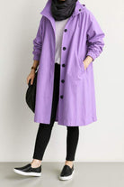 Water resistant oversized windbreaker in purple with hood and button closure worn with black leggings and sneakers