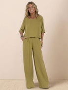 Woman wearing olive green short-sleeved pullover and wide trouser matching set against beige background