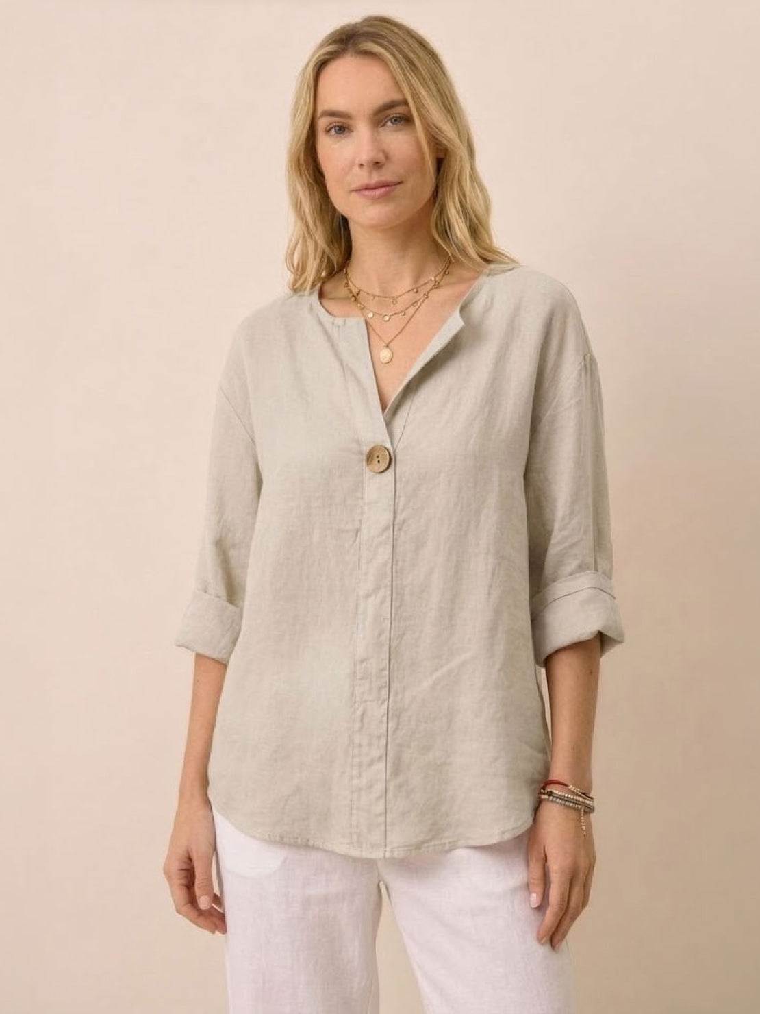 Woman wearing beige pure linen age-defying button detail shirt with rolled sleeves and white pants.
