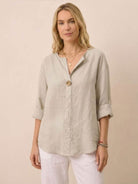 Woman wearing beige pure linen age-defying button detail shirt with rolled sleeves and white pants.