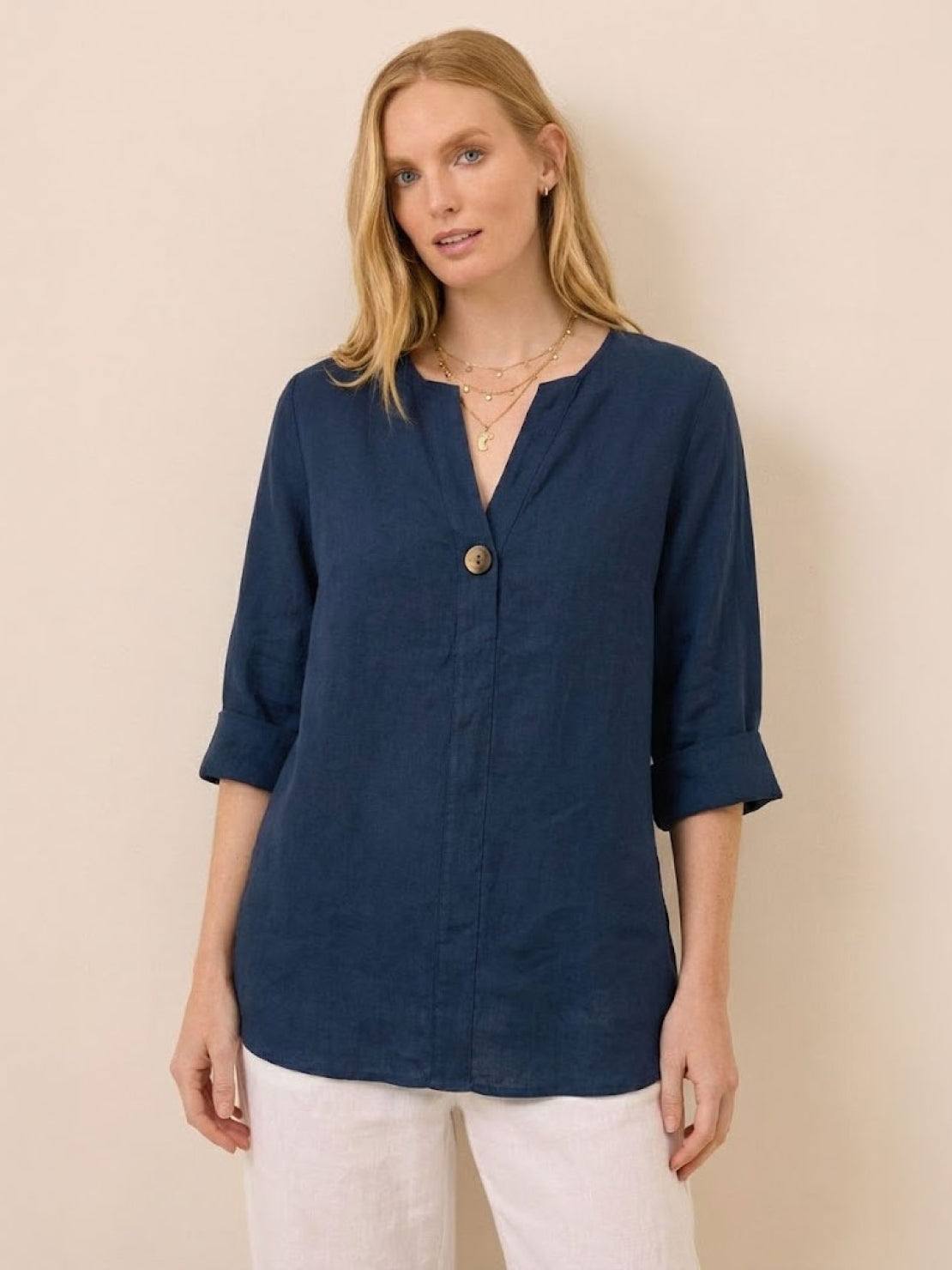woman wearing navy blue pure linen age-defying button detail shirt with three-quarter sleeves and white pants against beige background