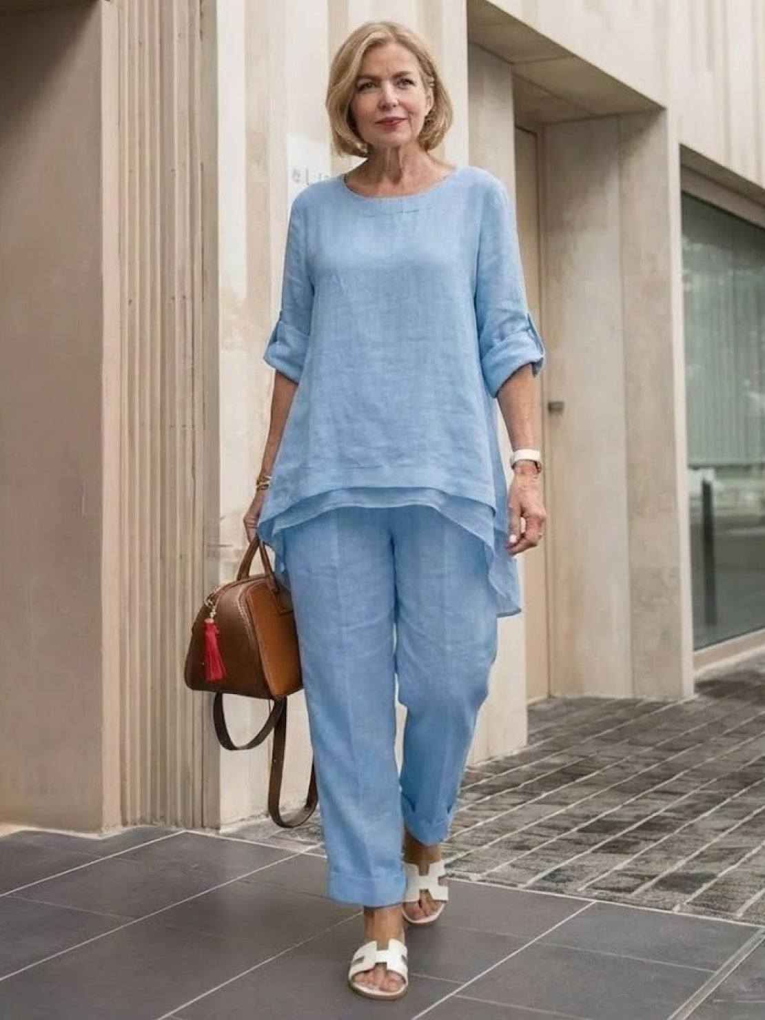 Woman wearing light blue asymmetrical two-piece trouser set with rolled sleeves and tapered pants walking outdoors