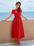 Woman wearing a capped-sleeve voluminous pleated midi dress in solid color with pockets and flattering drape