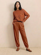 Woman wearing rust-colored European minimalism relaxed sweater top and matching trousers set with loafers against a neutral background
