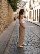 Woman wearing beige high-waist cotton linen palazzo pants with white tank top on cobblestone street