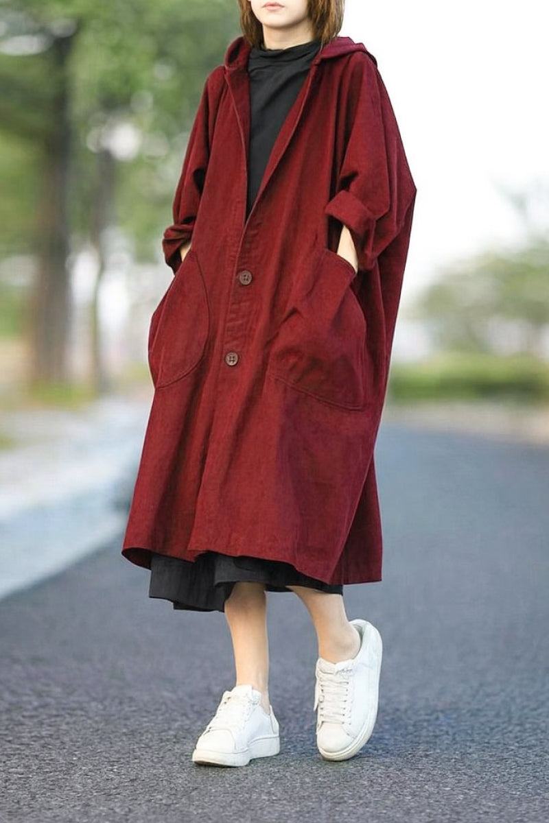Oversized heritage windbreaker jacket in burgundy with hood and large front pockets, worn with black dress and white sneakers.