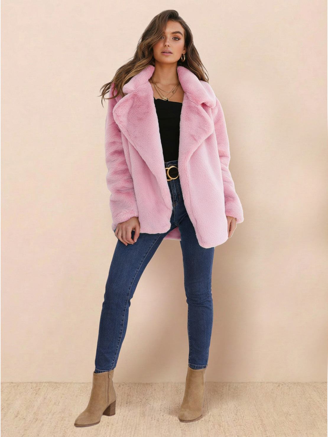 Woman wearing a pink open front oversized faux fur jacket with draped shawl collar, paired with black top, blue jeans, and beige boots.