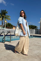 Woman wearing oversized linen shirt by pool with sunglasses and wide-leg pants