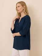 woman wearing navy blue pure linen age-defying button detail shirt with three-quarter sleeves and white pants