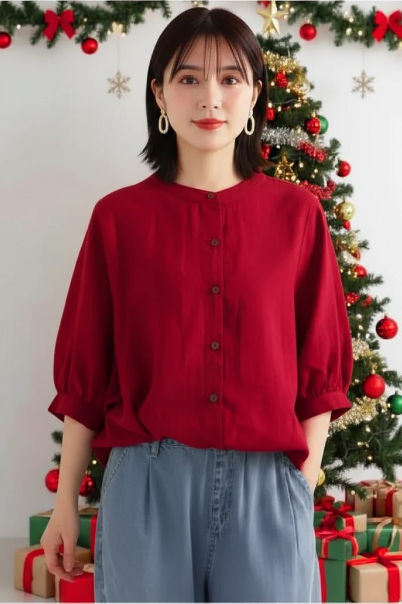 Woman wearing a relaxed loose breathable red linen blouse with button-down front in front of a decorated Christmas tree.