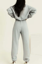 Woman wearing light grey cotton blend tracksuit with elastic waistband and cuffs, standing with hands on hips, back view