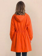 Woman wearing orange Rain Couture Windbreaker oversized water-resistant jacket with hood, back view
