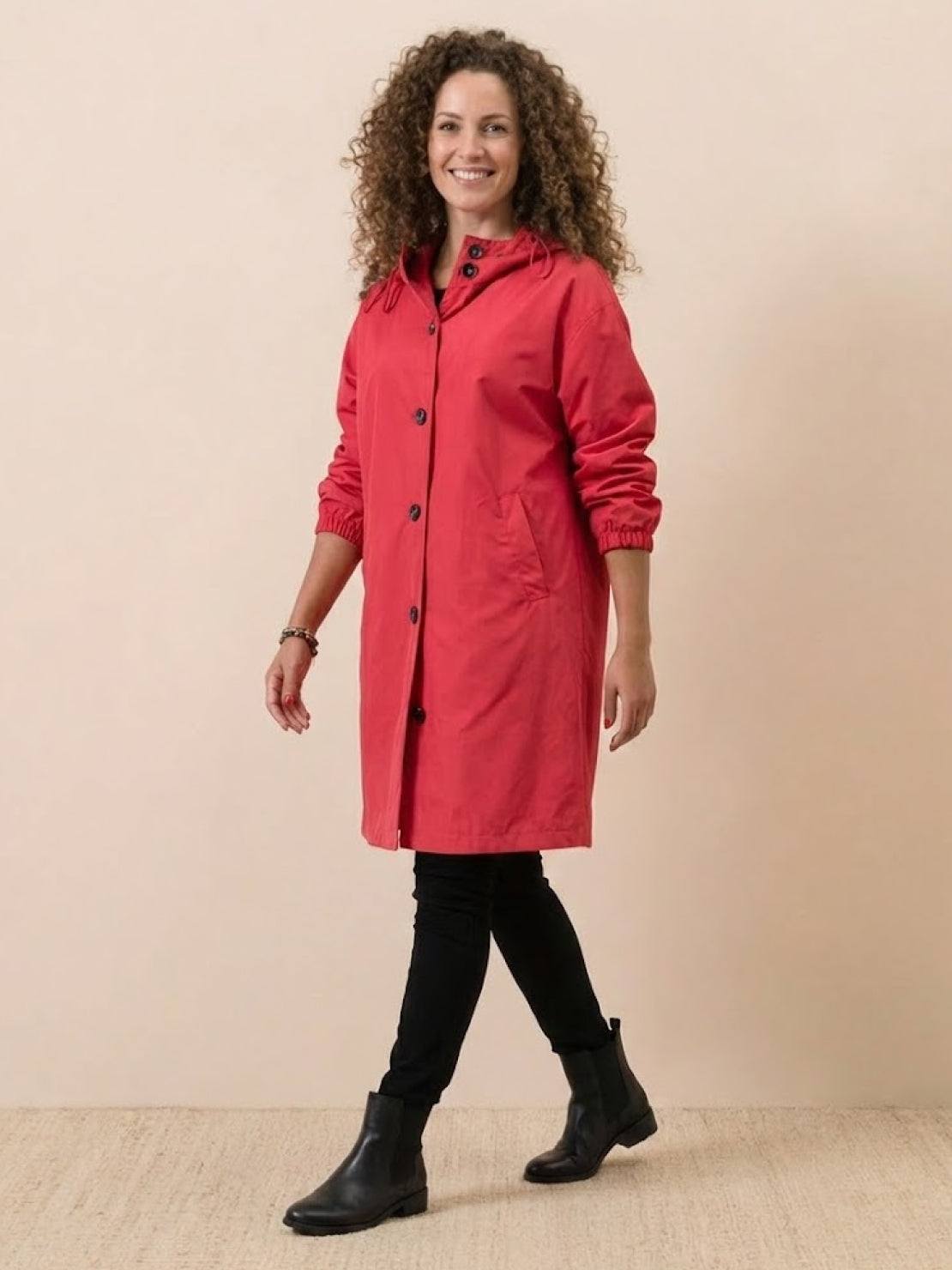 Woman wearing a red Rain Couture Windbreaker with oversized fit, water-resistant fabric, and black boots against a neutral background