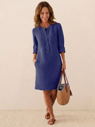 Woman wearing a casual blue cotton dress with rolled 3/4 sleeves and front buttons, carrying a woven bag.