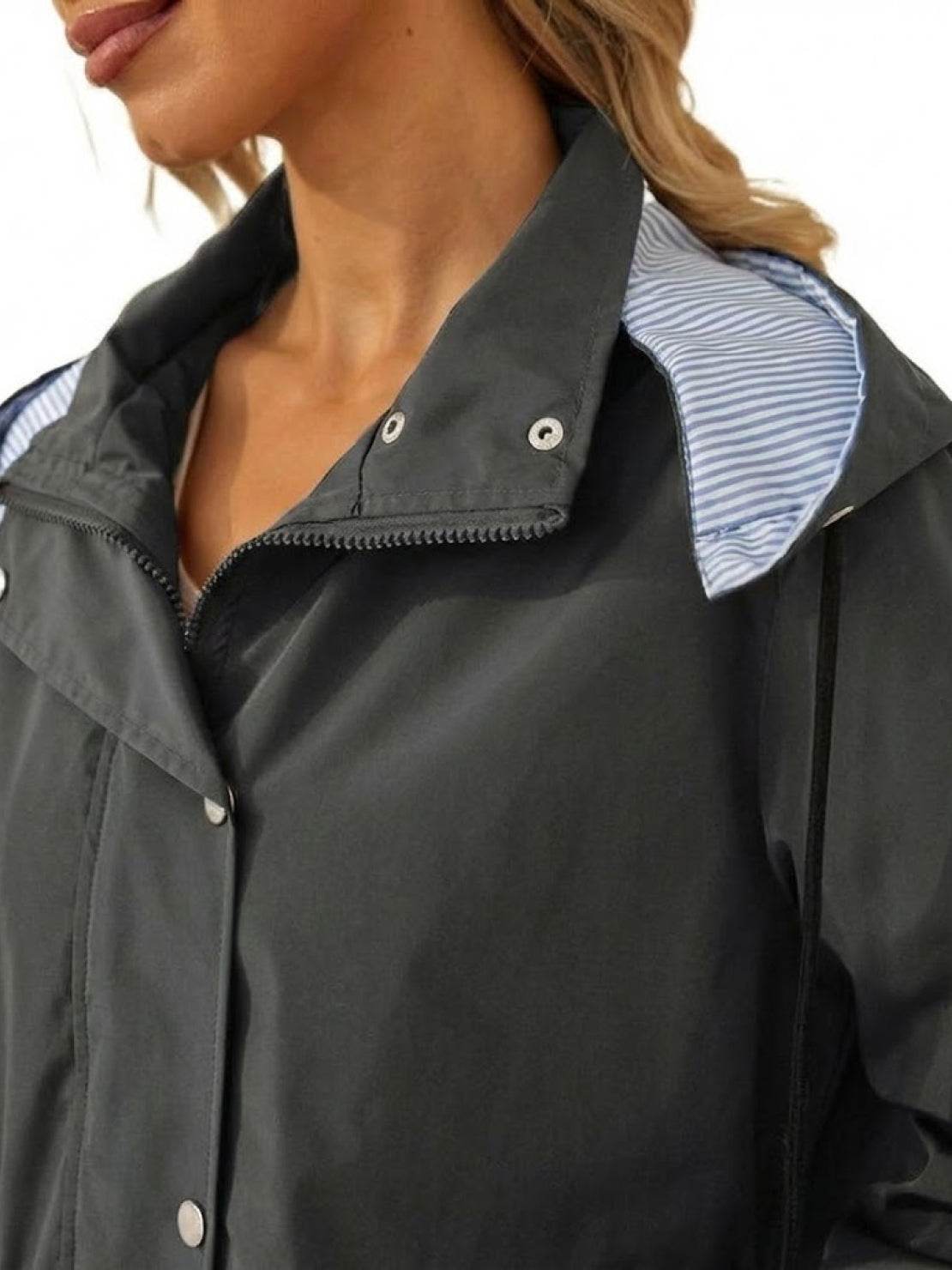 Close-up of woman wearing a black water resistant windbreaker with a hood showing striped inner lining and front zipper and snap buttons